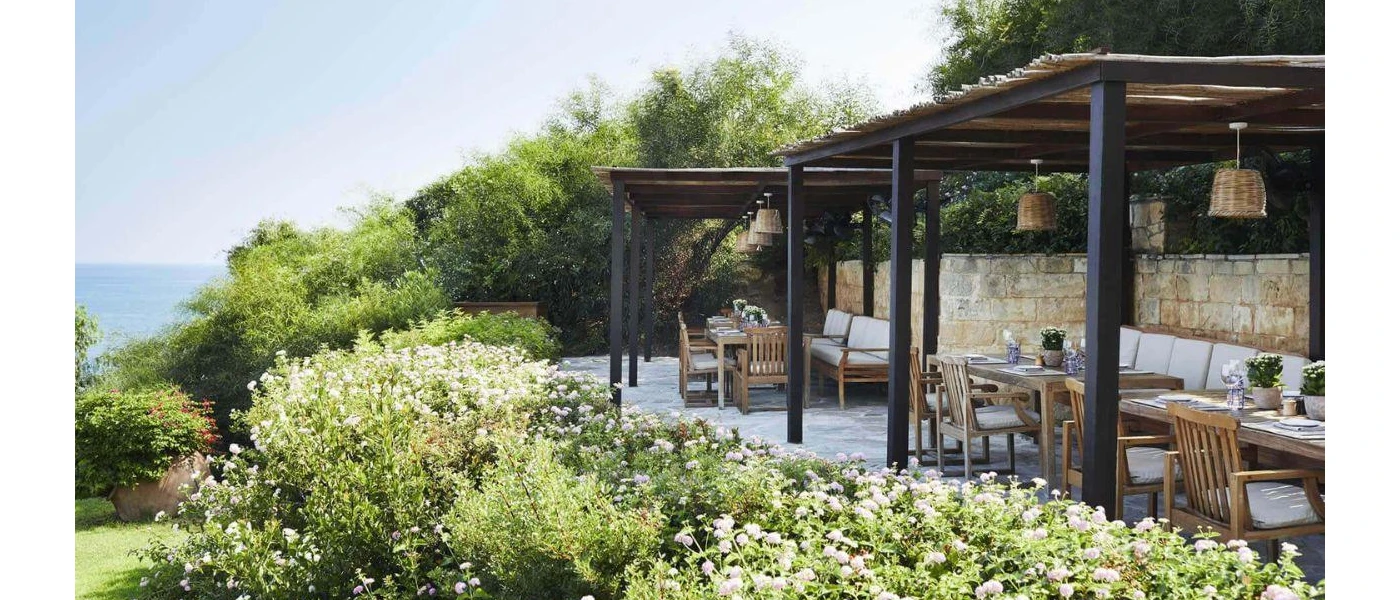 Wooden tables on an outdoor terrace with wooden pagodas and rattan lighting, and a view of greenery and the sea