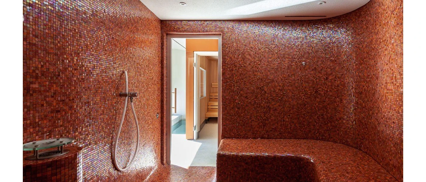 Wellness room covered in mosaic-style pink tiles, with a bench and shower head