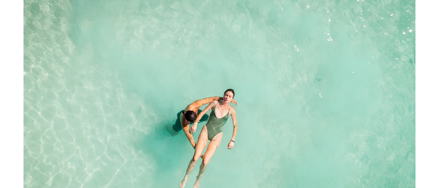 Woman in a grey swimsuit with her eyes closed floats on her back in water supported by a team member