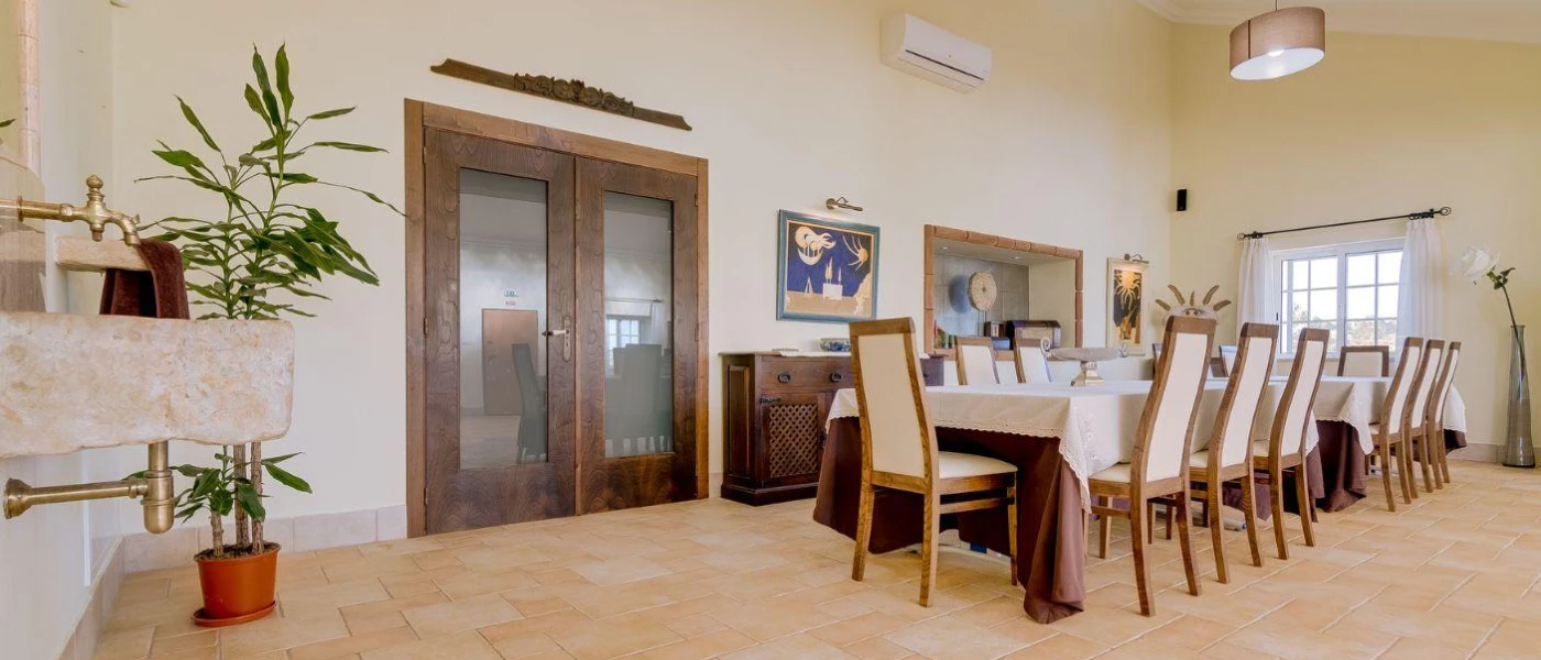 Airy restaurant with a long table with chairs, potted plants and neutral walls