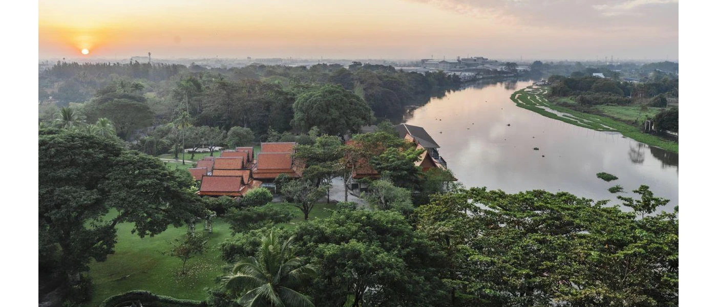 Terracotta-tiled rooftops peering out from tropical greenery next to a river at sunset