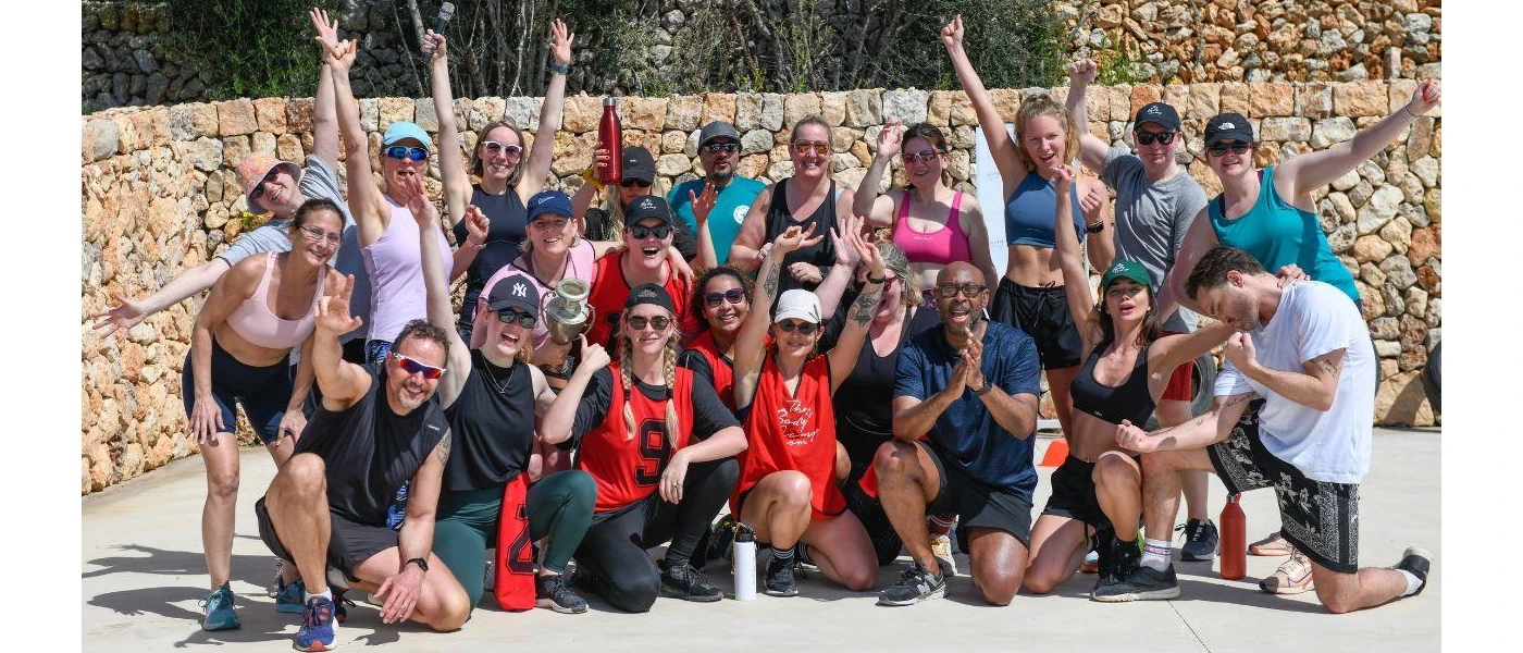 Smiling group in active wear raise their arms for the camera in a sunny courtyard