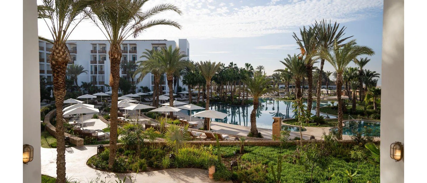 High-rise hotel building, swimming pool and palm-cloaked grounds under a blue sky