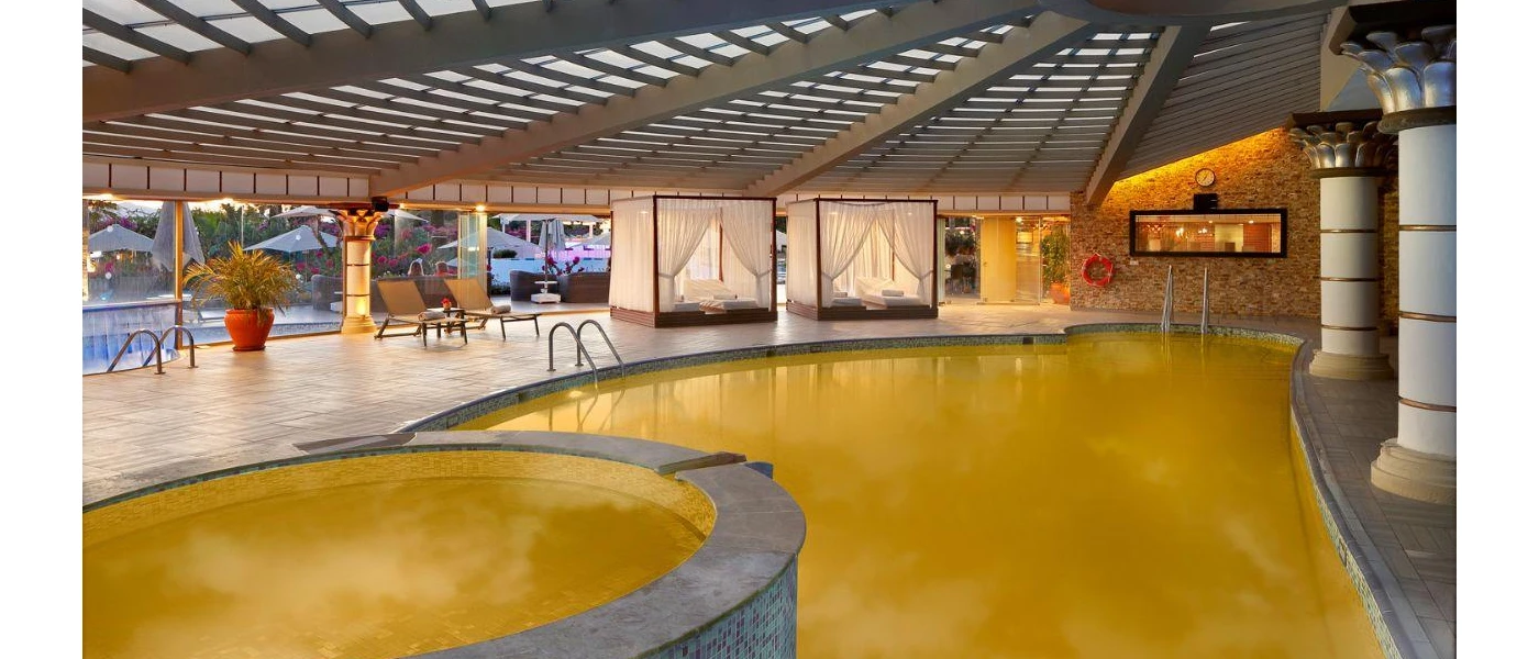 Indoor pool with lime green water in a room filled with columns, four-poster daybeds and full-length windows