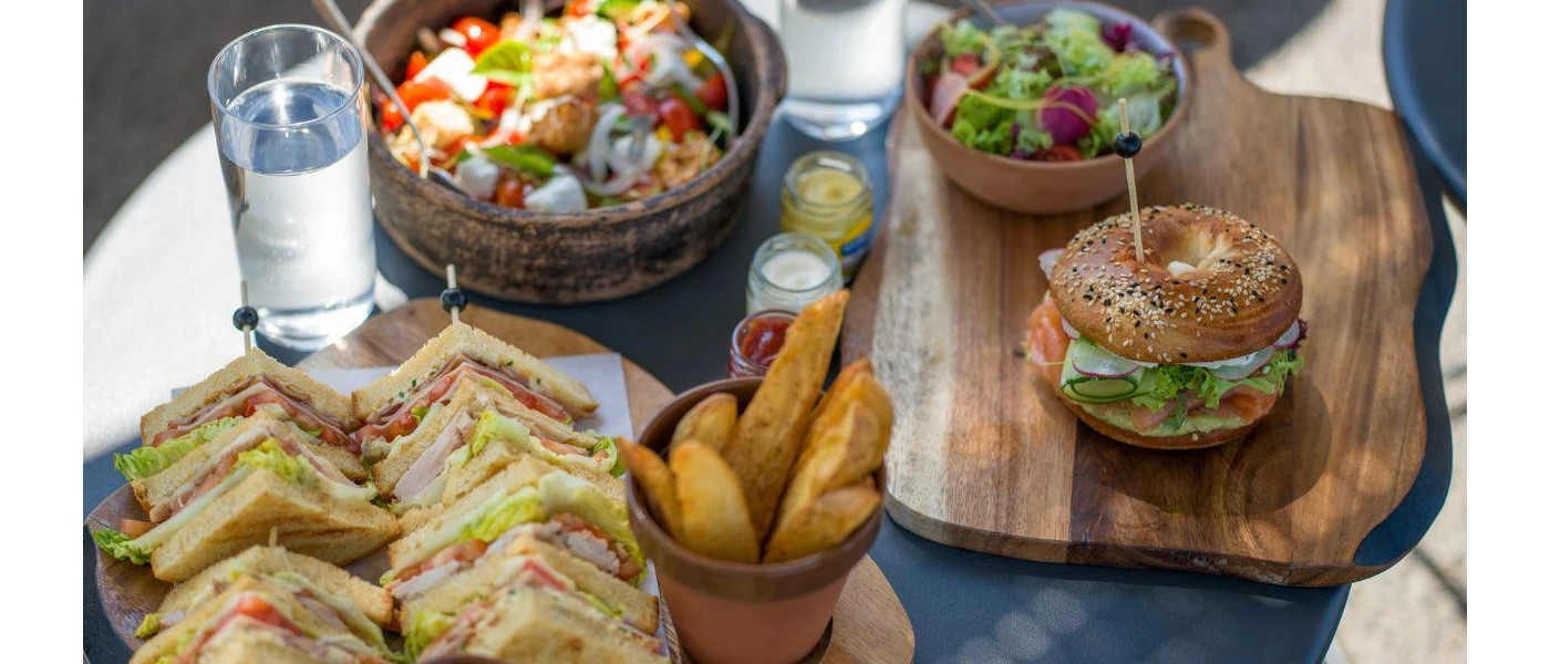 Spread of food - club sandwiches and chips, a bagel with salmon and salad, two bowls of salad and two glasses of water