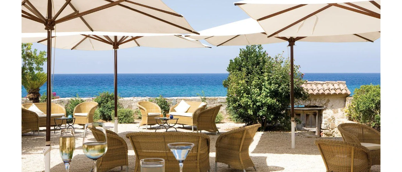 Sunny terrace with white parasols, rattan chairs and shrubs overlooking the sea