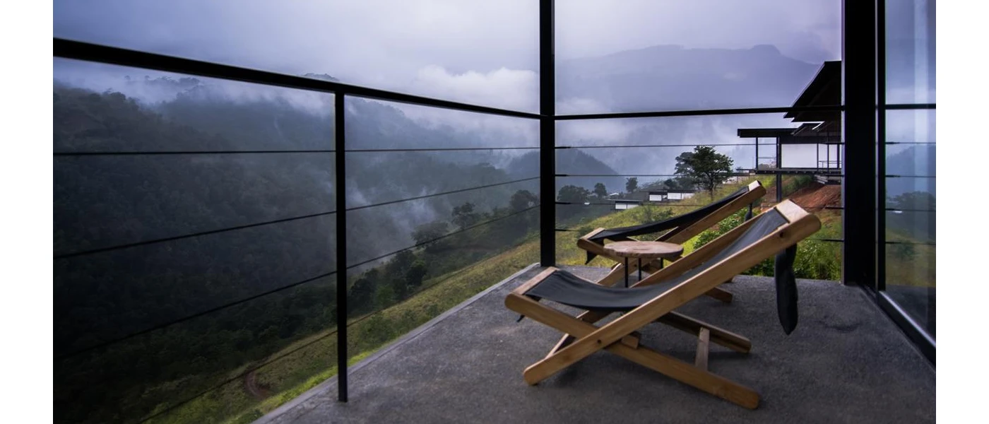 Balcony with dark deck chairs overlooking misty mountains and forested slopes