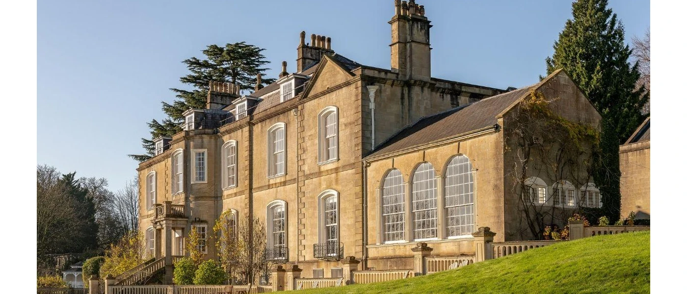 18th-century manor house surrounded by a grassy lawn and tall trees