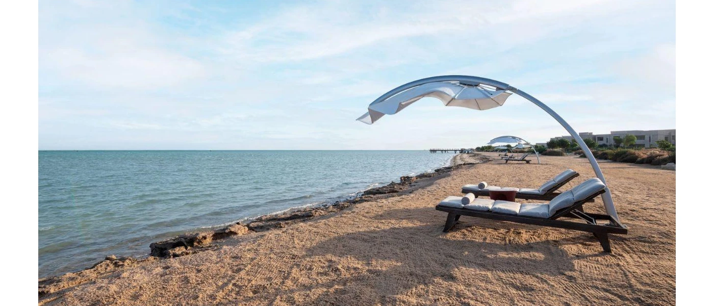 Wooden loungers with squidgy white cushions and a curved parasol over the top on the sandy shoreline
