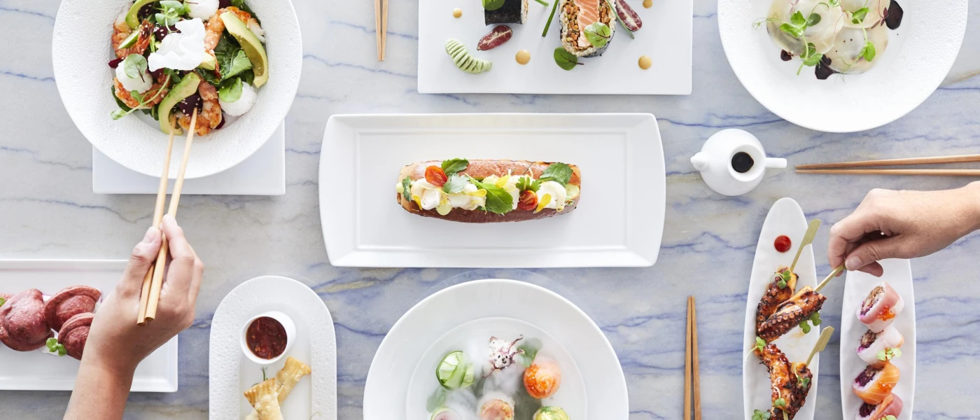 White plates and dishes piled with healthy looking, colourful cuisine, including octopus legs, sushi and stuffed pastry with a red sauce