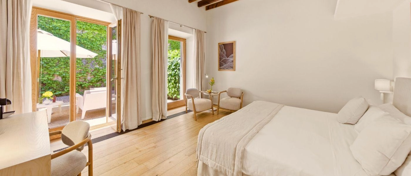 Neutral bedroom with white beddin. ivory seating area and double doors leading to patio
