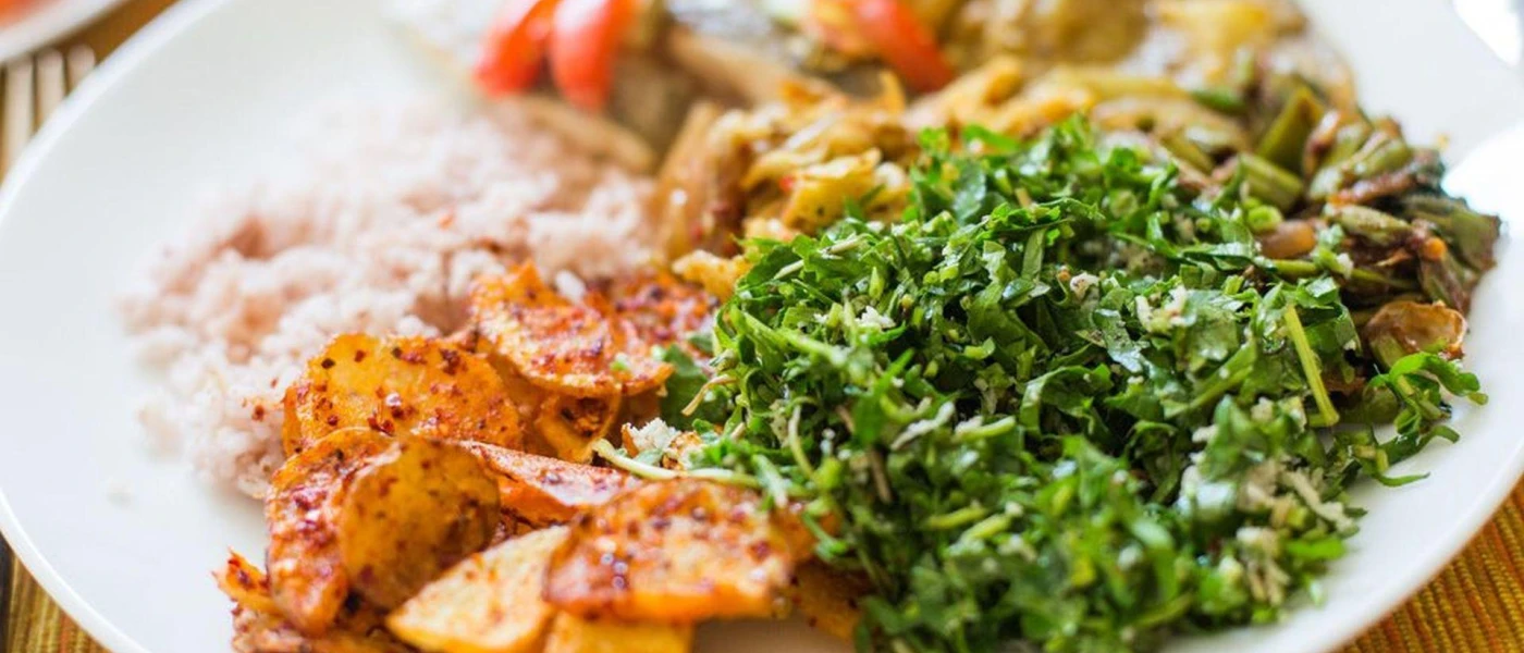 White plate with colourful food, including green vegetables and potatoes coated in a red spice