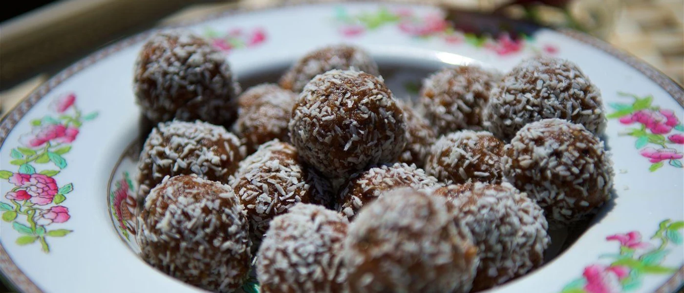 Brown coconut-dusted protein balls in an elegant floral china bowl