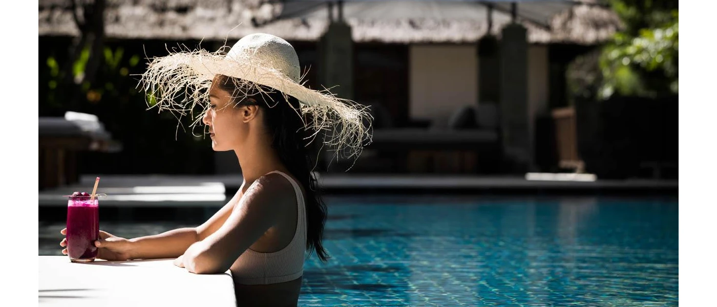 Woman in a straw hat in a swimming pool with a purple coloured juice 