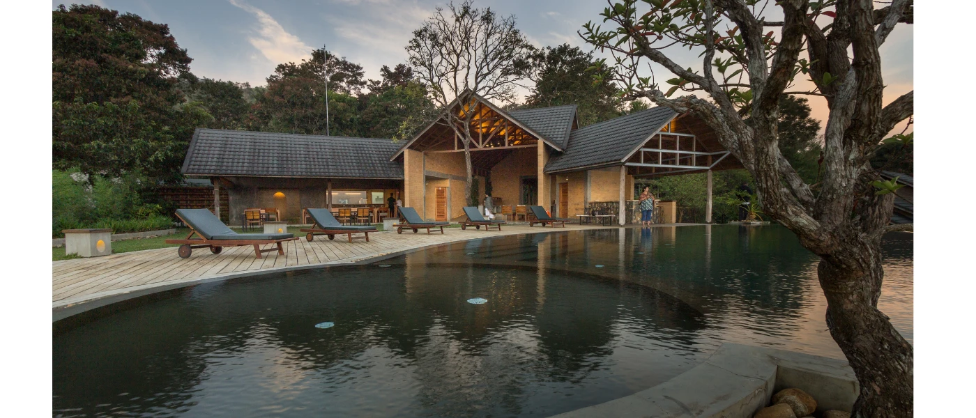 Wooden building with triangular tiled rooftops overlooking a pool and whirlpool section with loungers lined up along the edge