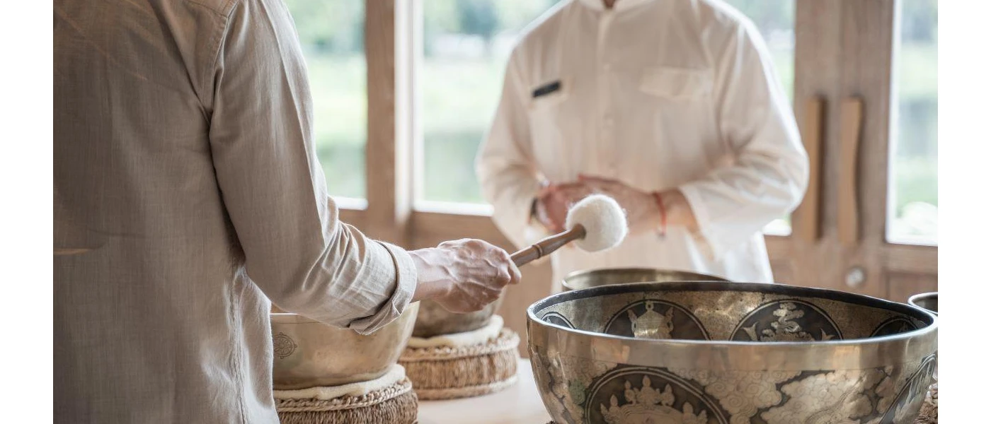 Two people in white loose fitting clothes stand over sound bowls