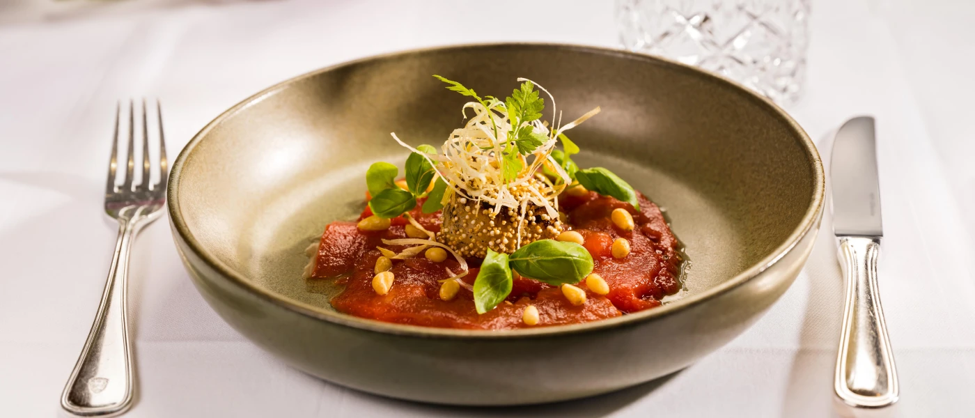 Dark bowl plated with nutritious looking food, including a tomato puree and corn, garnished with herbs