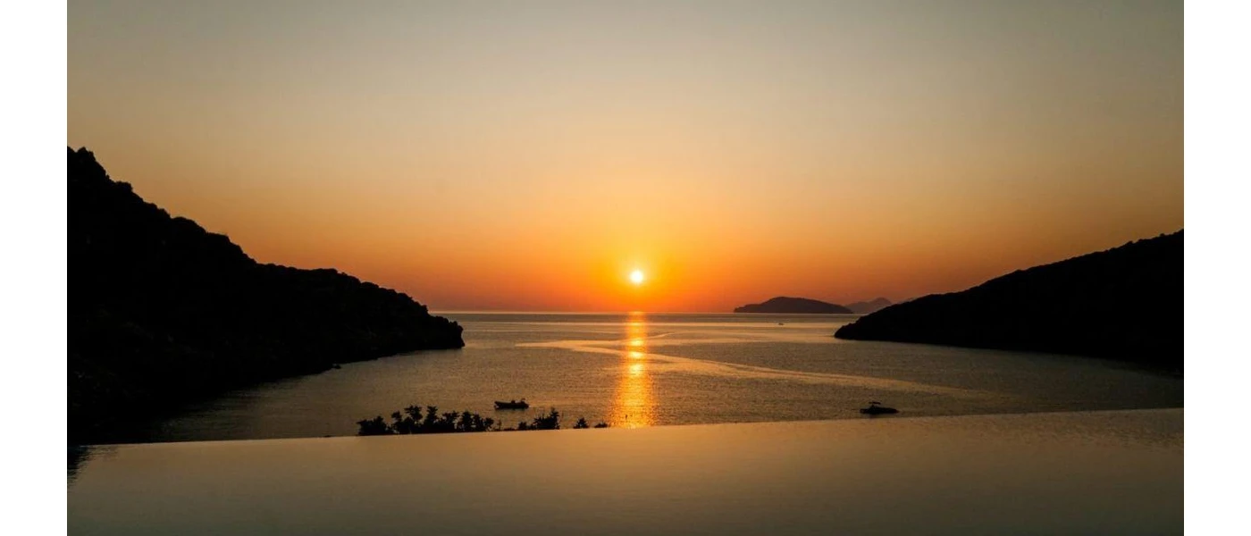 Infinity-edge pool with a view of the sea and surrounding hillsides and the sun setting over the horizon