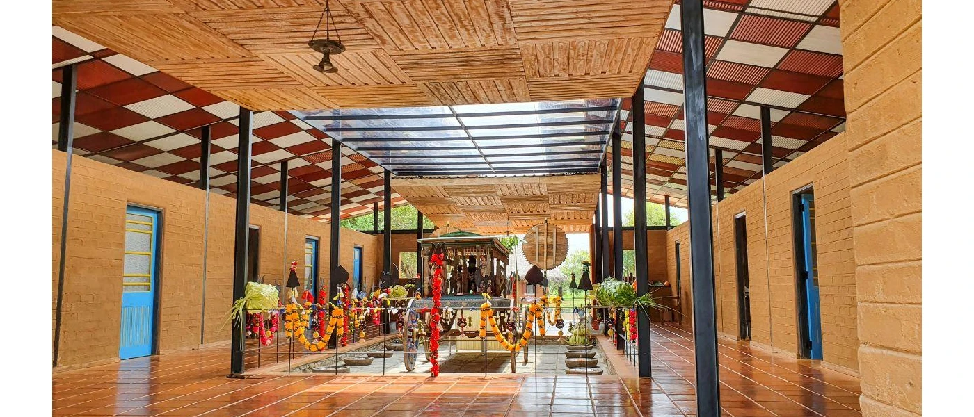 Room with tiled floors, a wooden ceiling and a glass-walled courtyard, with colourful flower chains draped over it