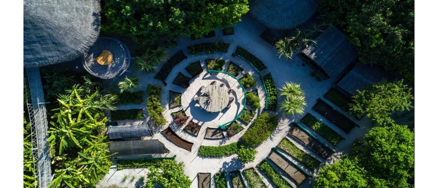 Aerial view of thatched villas and plant beds in a circular design, with a table at the centre