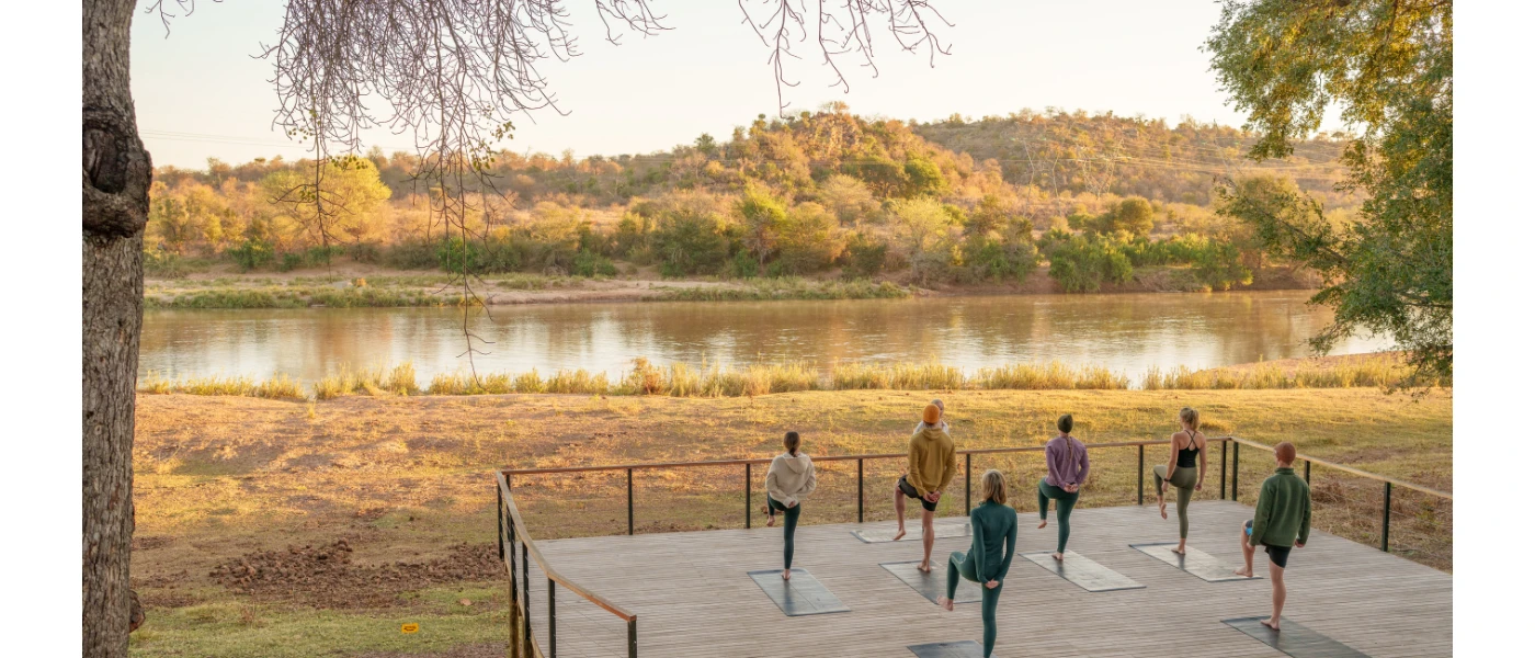 Group participate in a class on a wooden deck overlooking a river and thick greenery