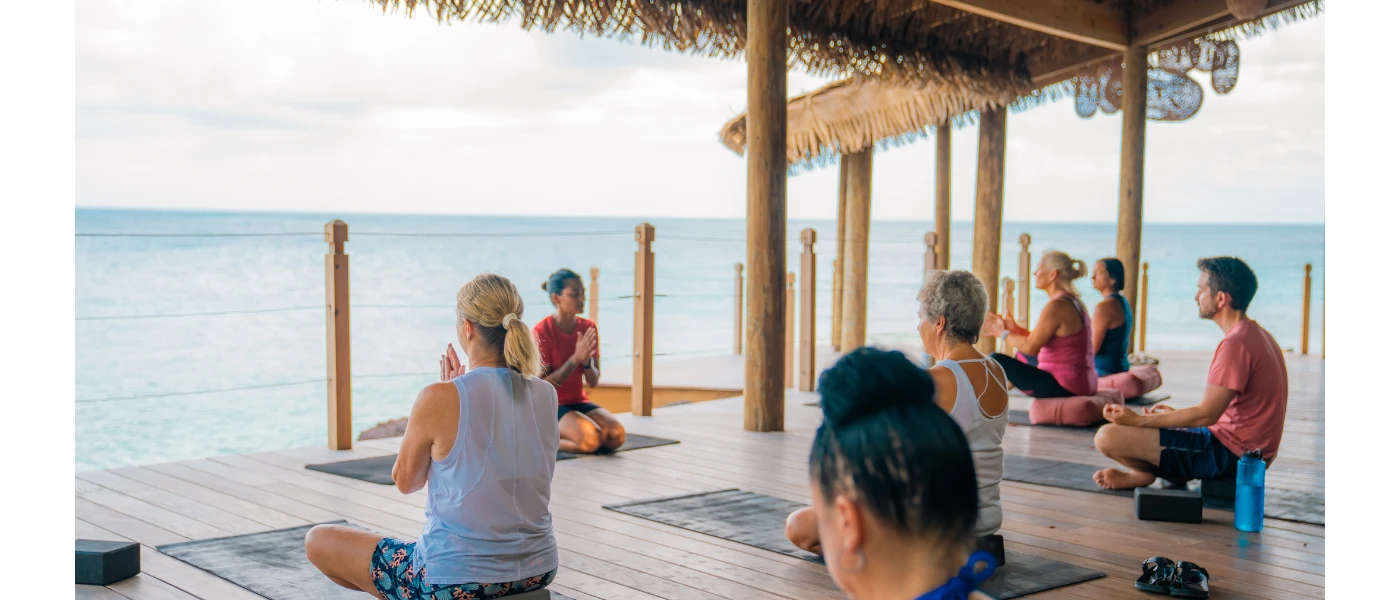 Group practice yoga on a wooden deck under an ocean-facing thatched-roof pavilion