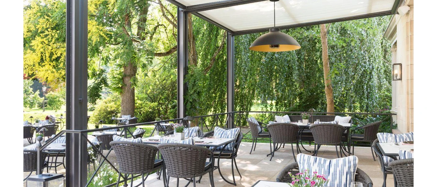 Open-air restaurant terrace among gardens, with grey rattan chairs and blue, white and grey cushions
