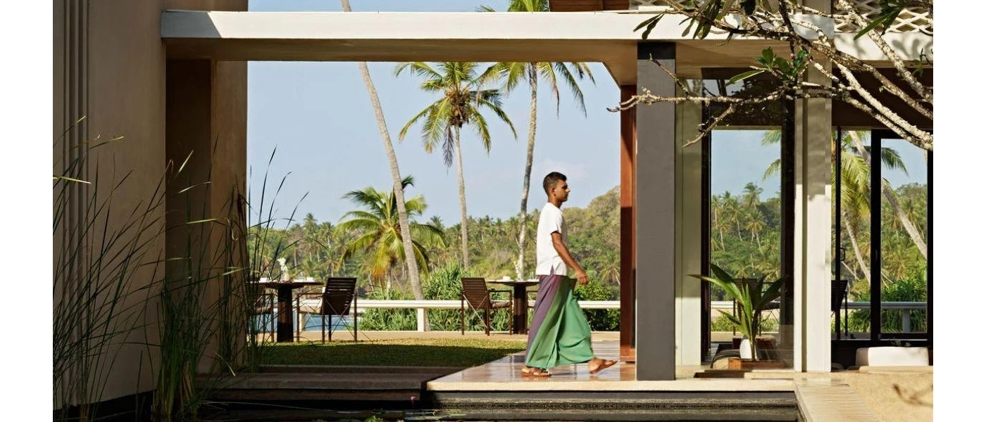 Man in traditional dress walking through an open-air furnished terrace overlooking tropical palm trees and greenery