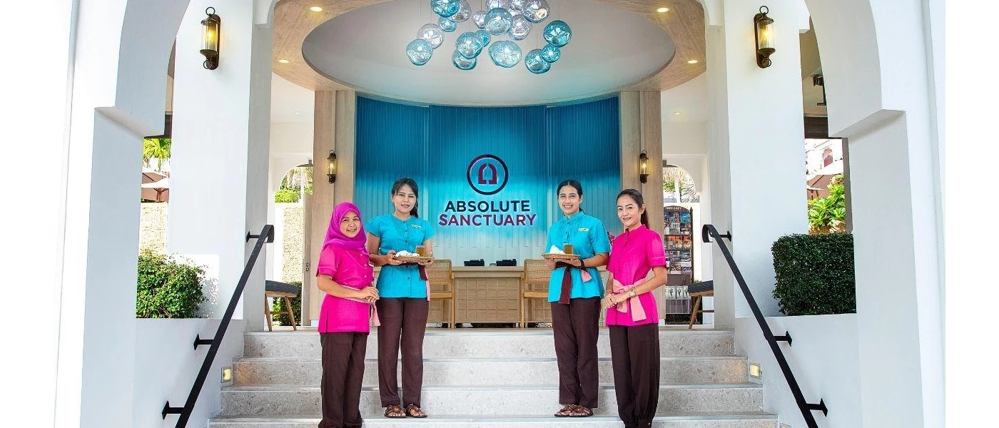 Smiling staff in pink and blue uniforms stand on the steps at the entrance to Absolute Sanctary, with contemporary hanging blue lights overhead