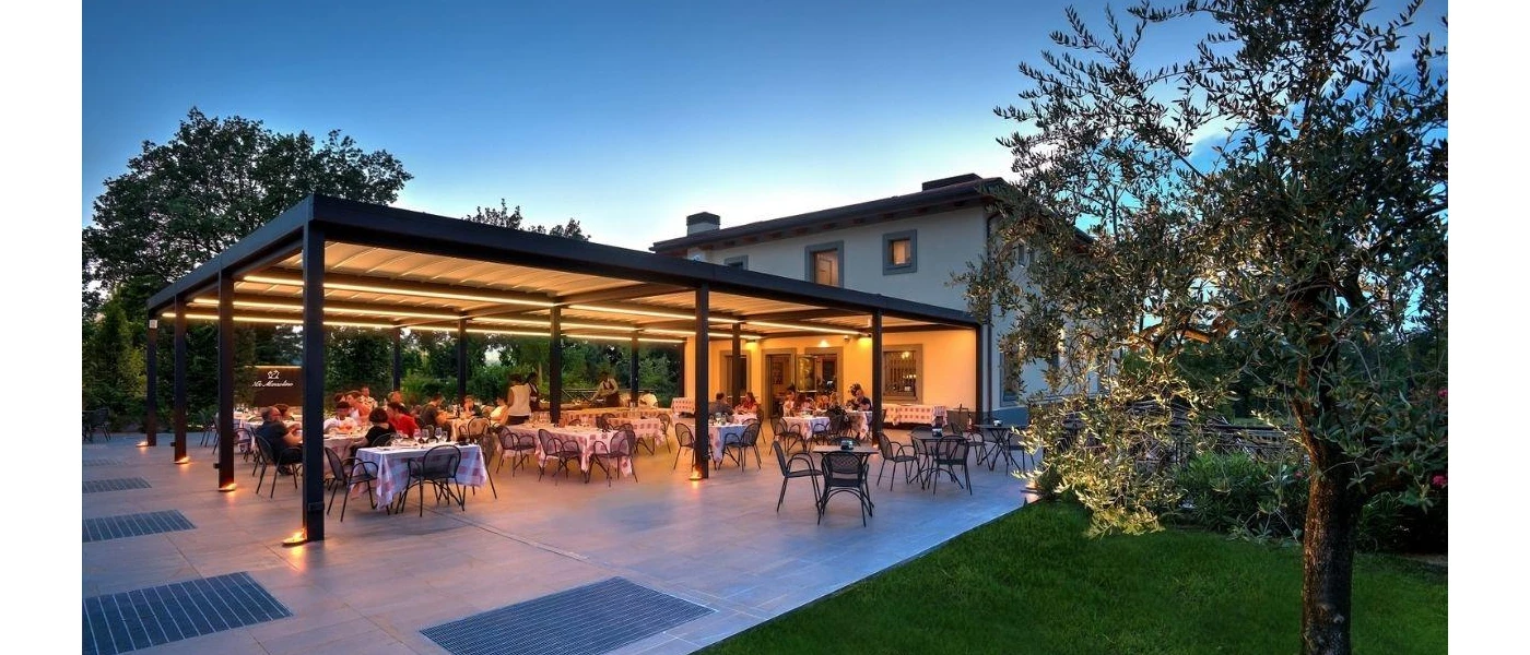 Outdoor restaurant terrace full of diners, with red and white chequered tablecloths, next to a grass lawn