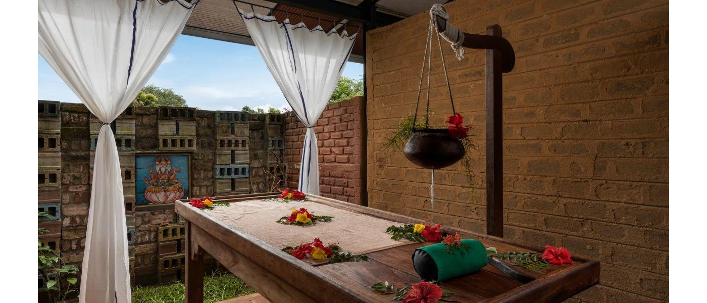 Open-air treatment room with a wooden bed, white drapes and colourful flowers