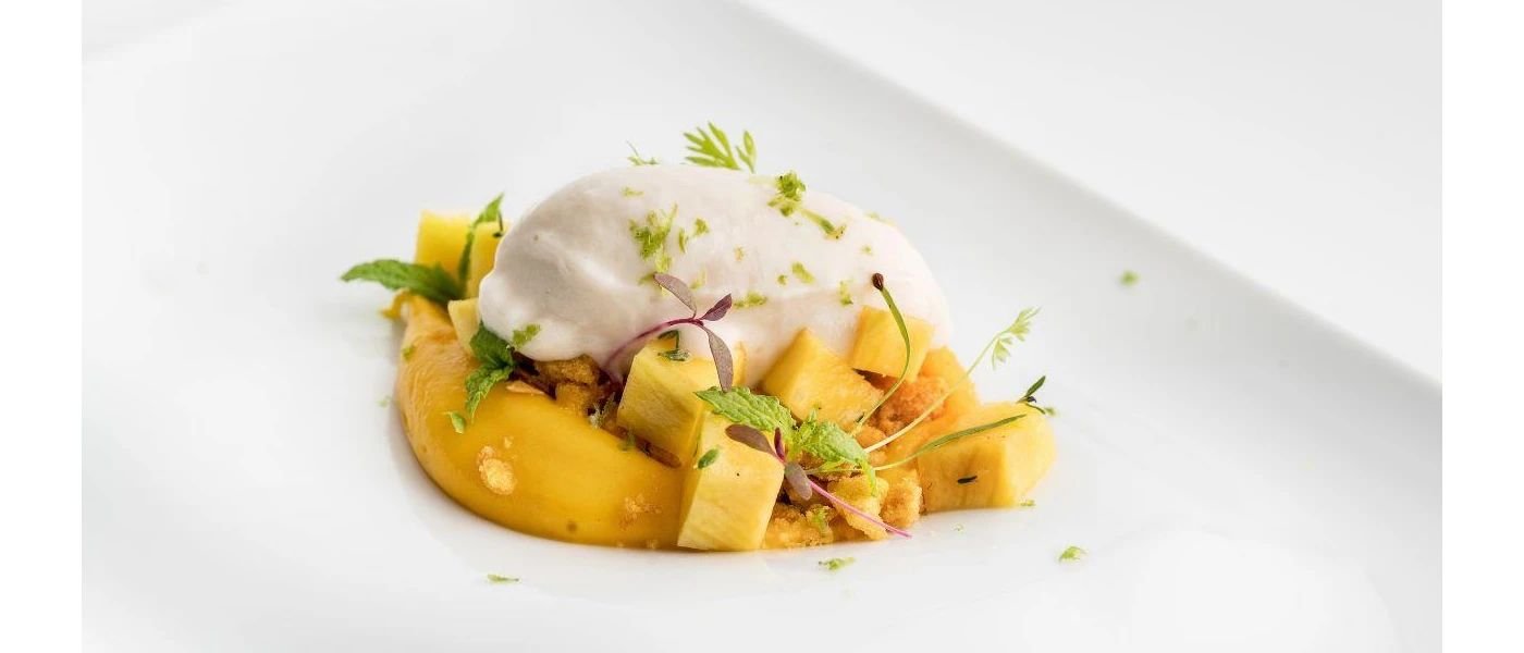 White bowl with yellow vegetables, topped with a yoghurt-like sauce