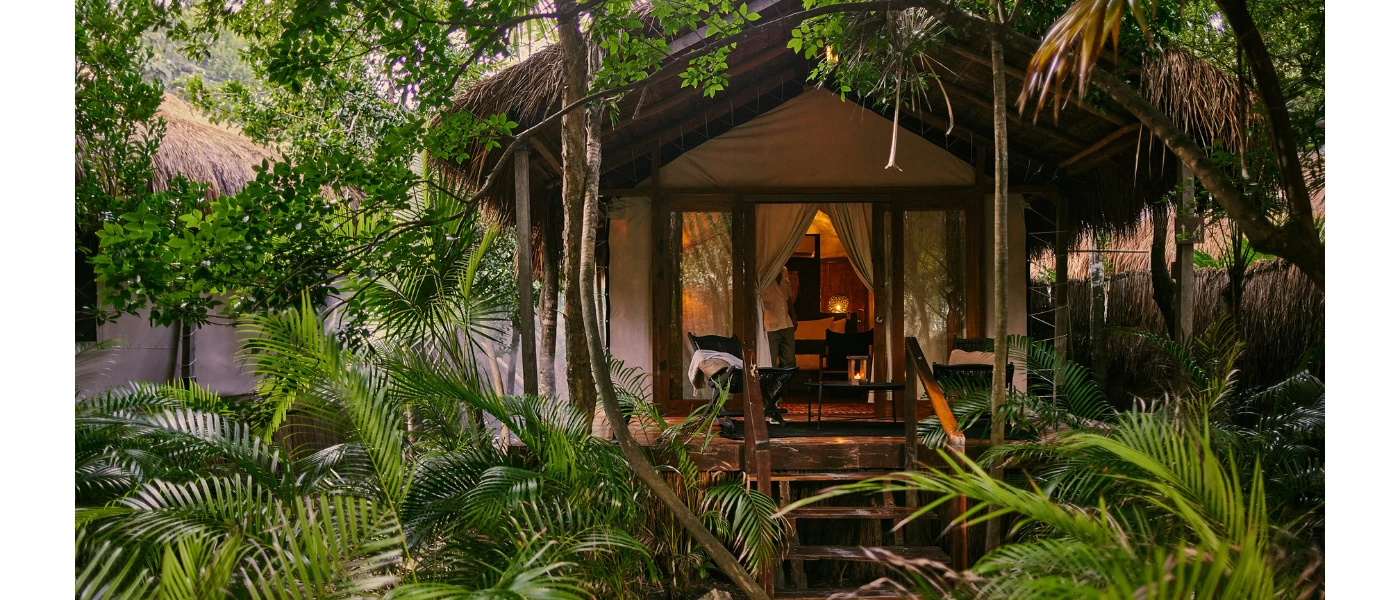 Lodge-style accommodation in the jungle, with a palapa roof and full-length terrace doors that show white drapes inside