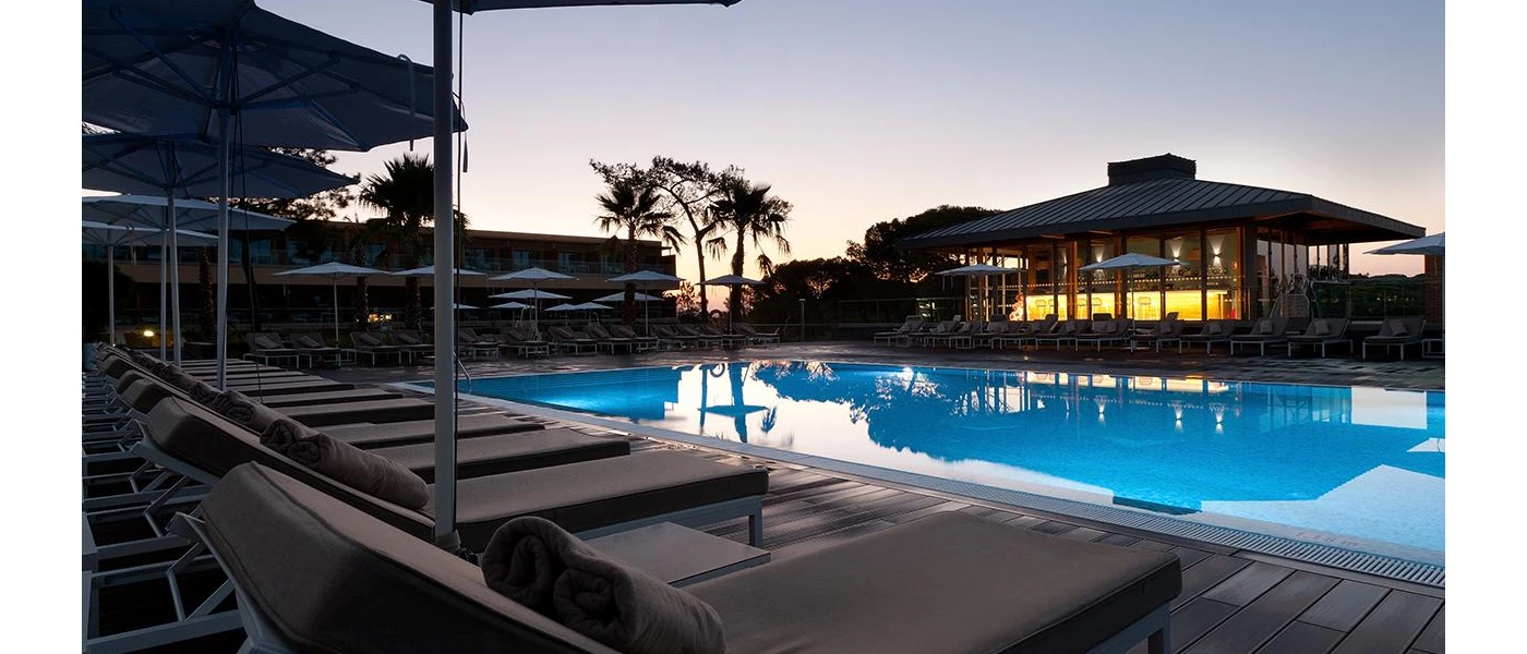 Wooden terrace with a swimming pool and grey-cushioned loungers at twilight