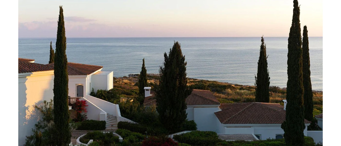 Whitewashed buildings with terracotta roof tiles, surrounded by cypress trees and with a sea view 