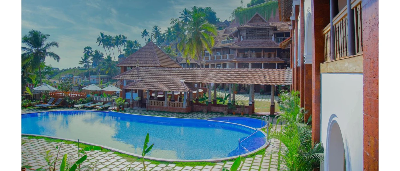 Curvy swimming pool in a stone terrace lined with white loungers and parasols surrounded by traditional Indian architecture