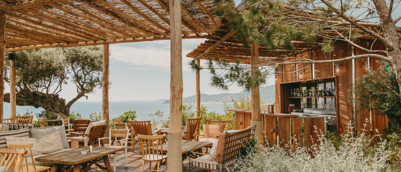 Rustic beach bar with wooden tables and chairs, neutral cushions and views of the sea 
