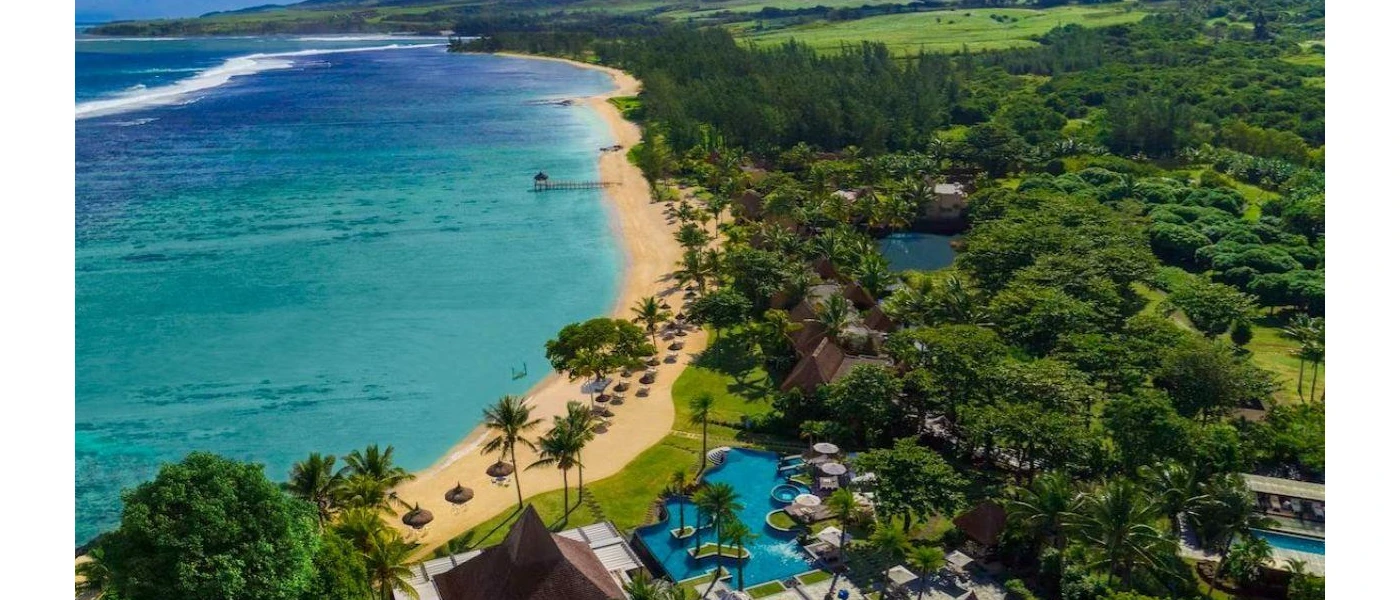 Aerial view of a tropical resort, with palm trees, a golden beach, thatched umbrellas and swimming pools