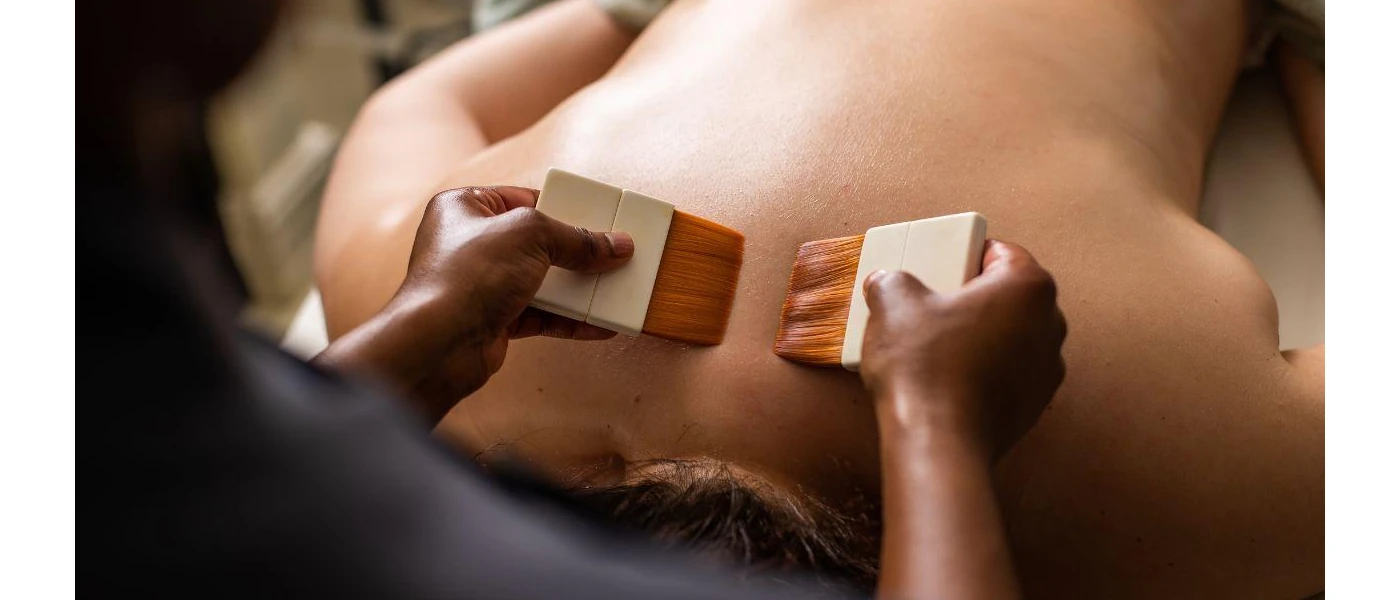 Person lying down as a therapist works on their back with paintbrush-looking tools