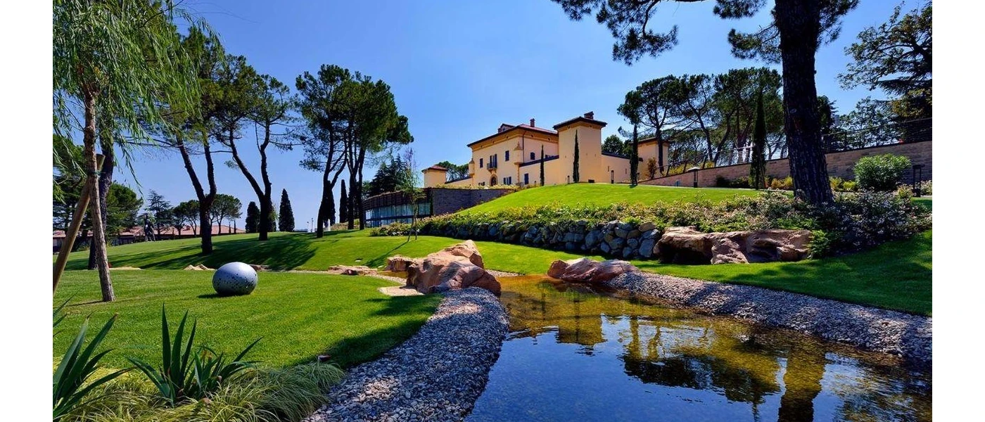 Italian villa with a terracotta roof and green window shutters overlooked manicured grounds and a stream