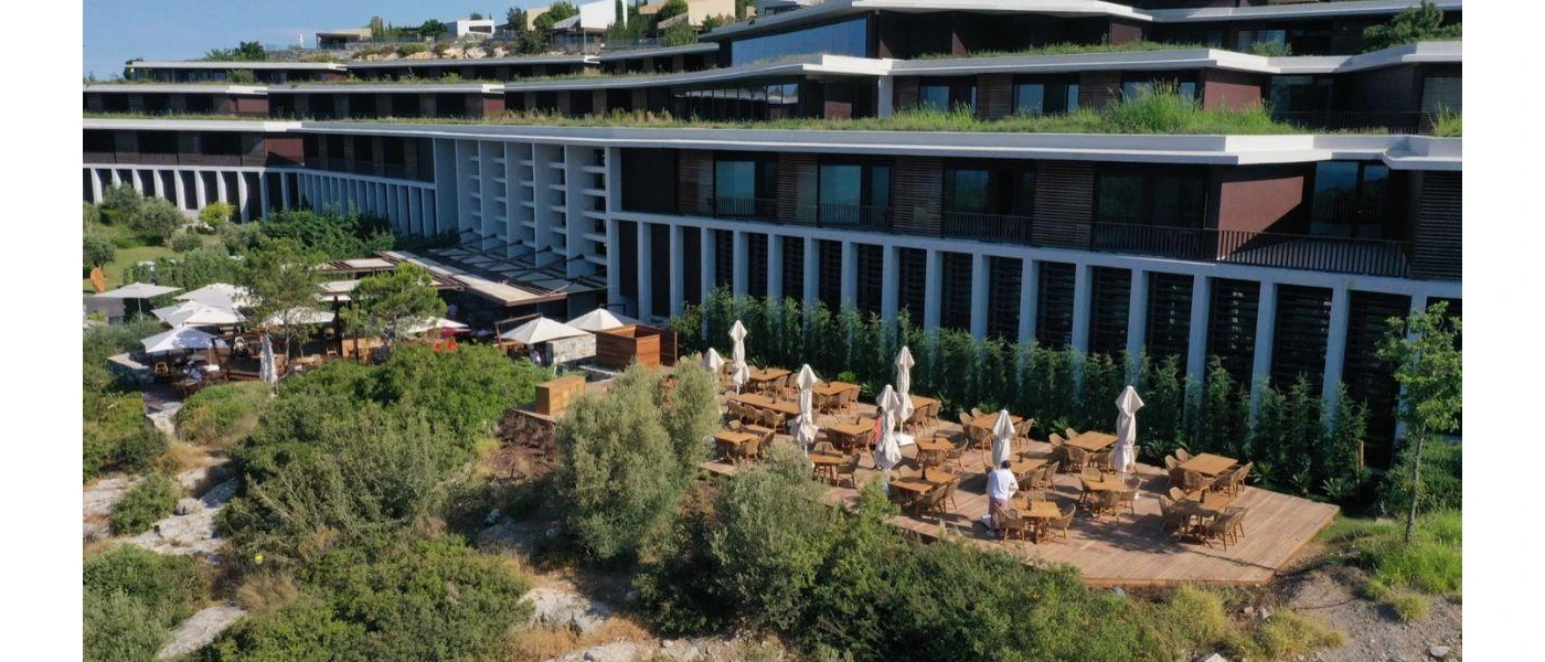 Furnished outdoor terrace among greenery, overlooked by a sleek building 