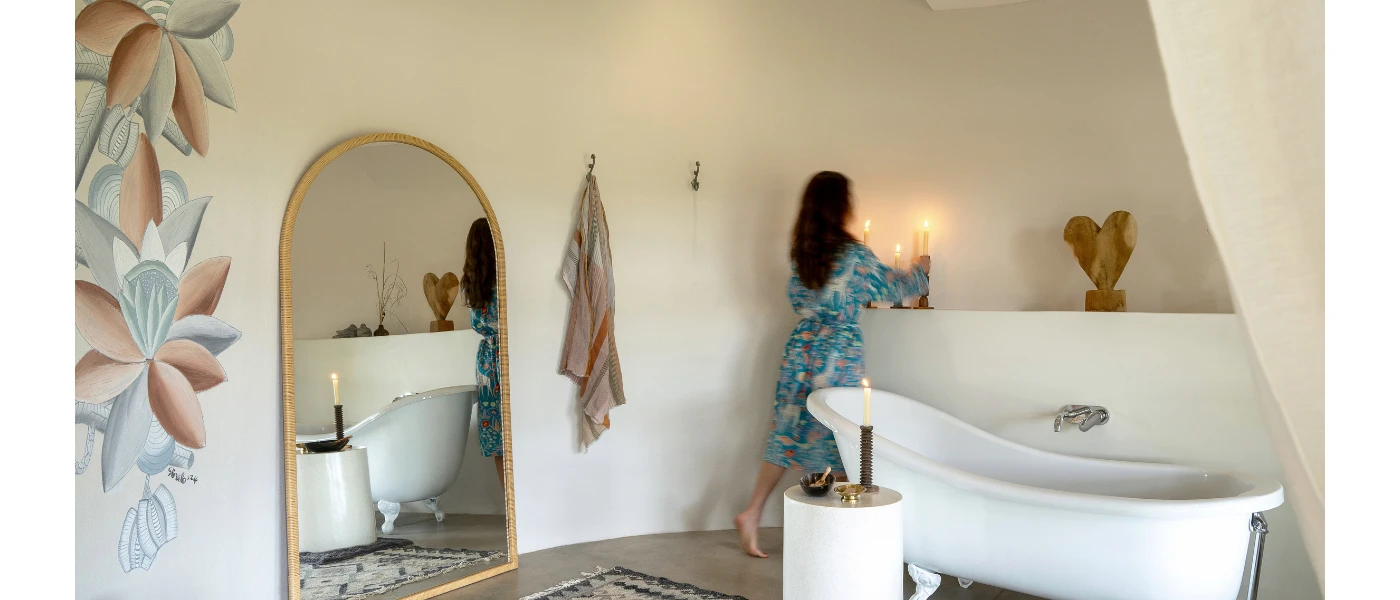 Luxe rustic bathroom with white walls, a freestanding bath, wooden sculptures, an arched mirror and floral wall murals