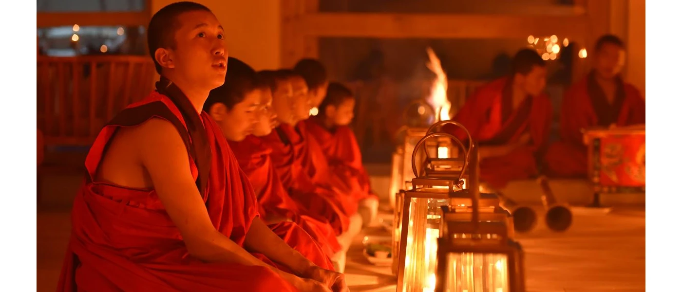 Monks in red robes sitting among lanterns and a fireplace