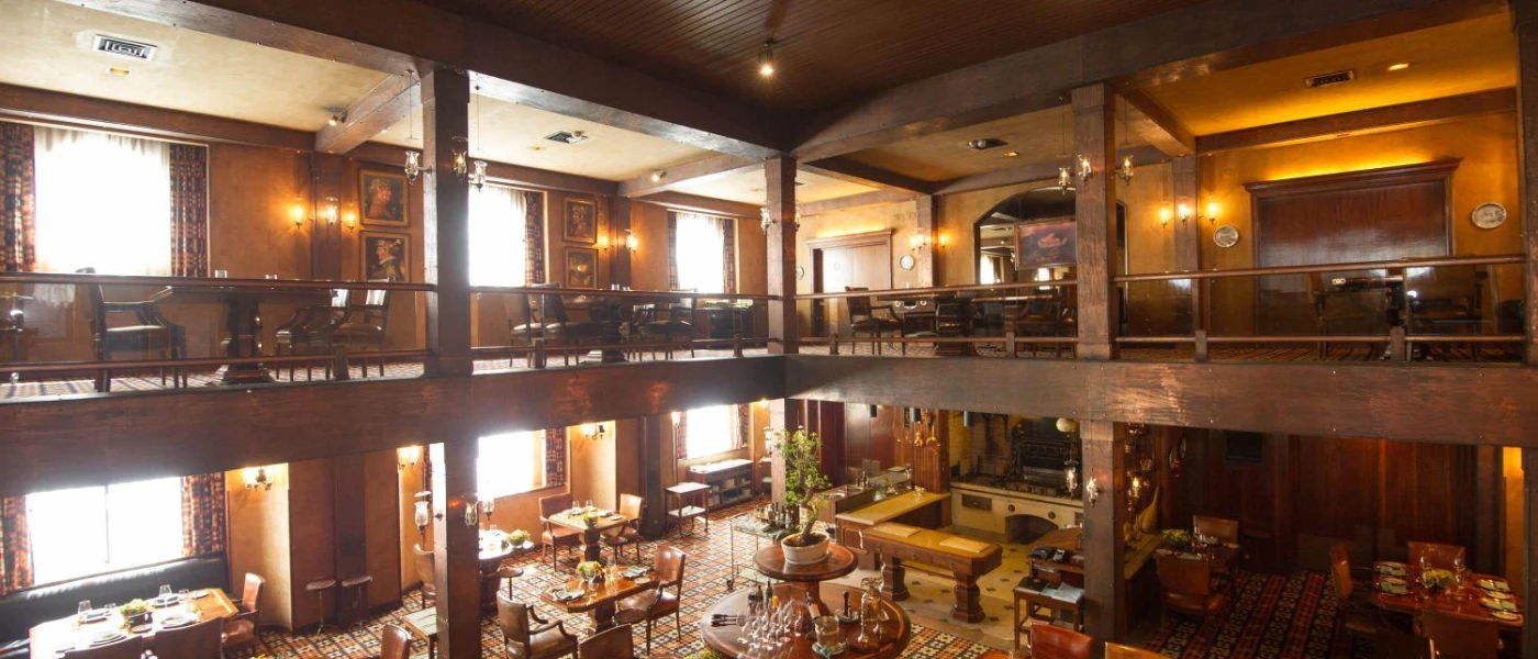 Elegant two-storey restaurant dressed in dark woods with tall pillars, a patterned carpet and soft lighting