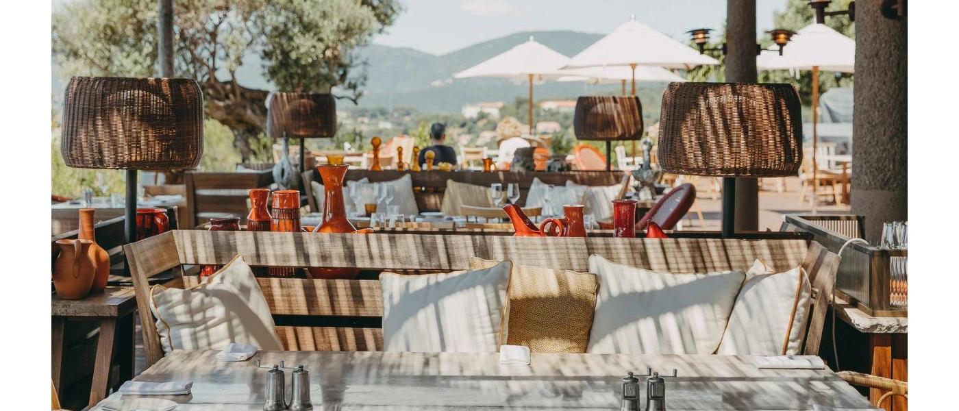 Rustic wooden sofa with neutral cushions, surrounded by terracotta pots and rattan lighting, with white umbrellas in the background