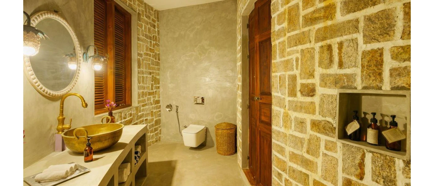 Rustic bathroom with stone walls, a wooden door and window, and a vanity unit with a large gold sink and mirror
