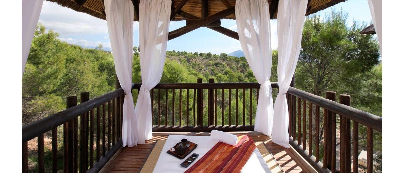 Wooden terrace with white drapes, a mattress, pillow and yoga mat with tropical forest surrounds