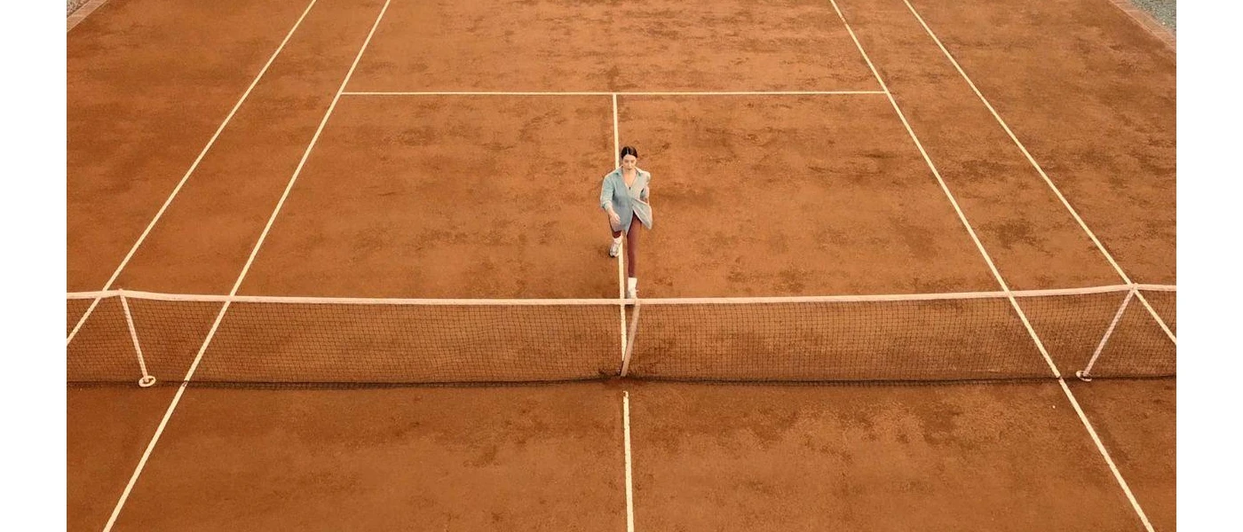 Lone figure in active wear on an orange tennis court