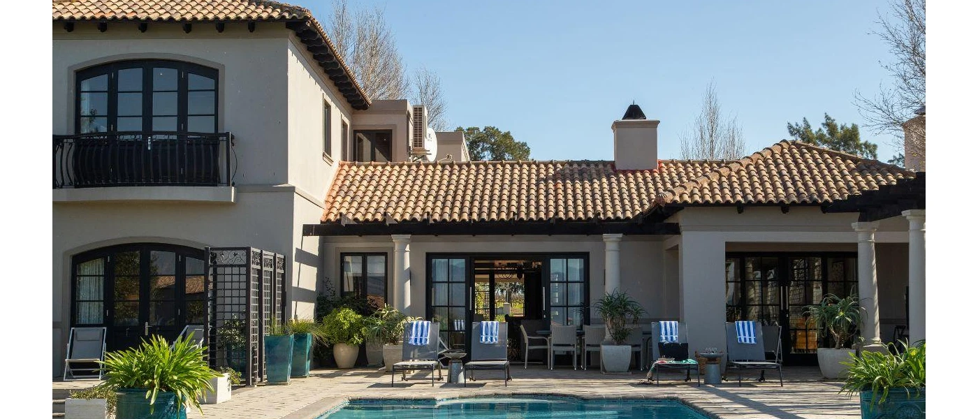 Terracotta-roofed villa with a private pool, surrounded by blue potted plants, and grey loungers with blue and white striped towels