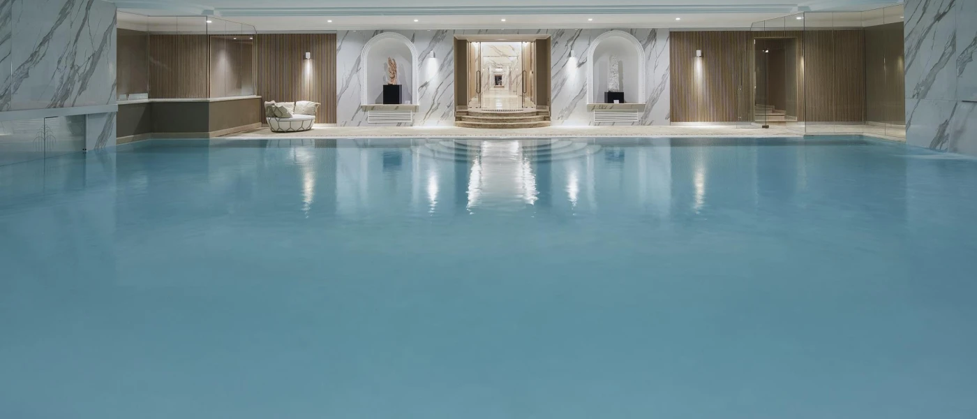 Indoor swimming pool surrounded by marble and wooden walls and with spotlights in the white ceiling